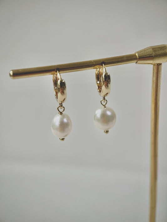 Gold hoop earrings with pearl drops on a gold stand against a light gray background