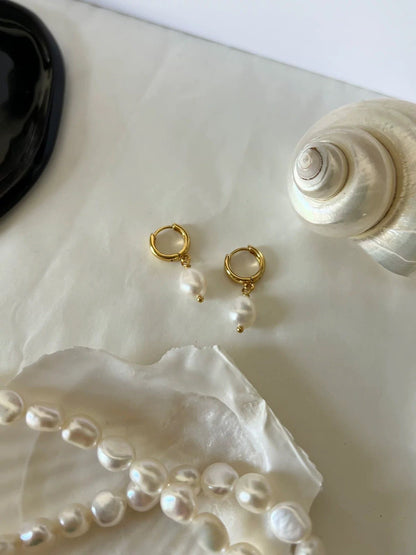 Gold hoop earrings with pearls on a shell and pearl necklace background