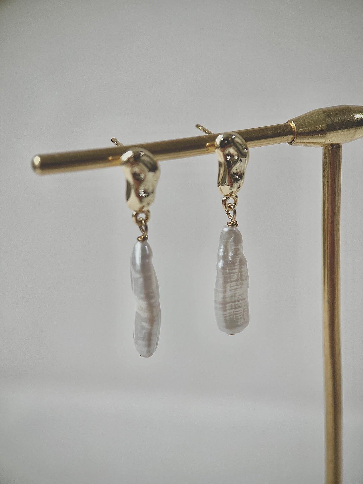 Pair of earrings with strip-shaped pearls on a gold stand against a gray background