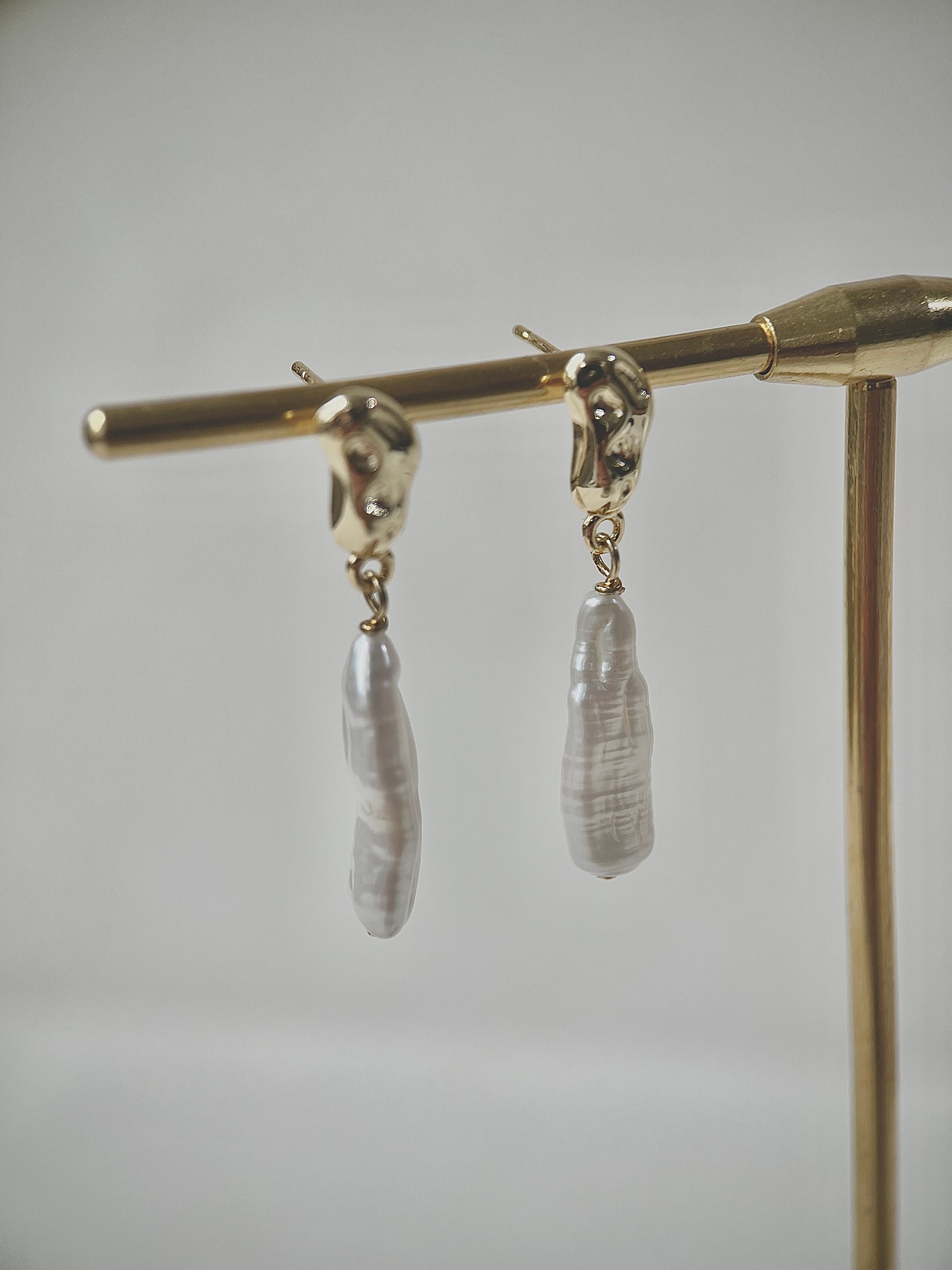Pair of earrings with strip-shaped pearls on a gold stand against a gray background