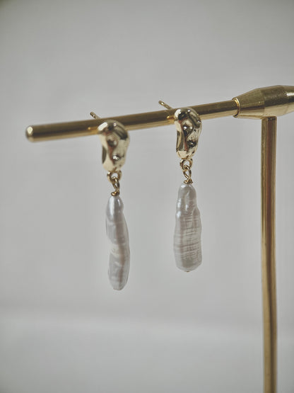 Pair of earrings with strip-shaped pearls on a gold stand against a gray background