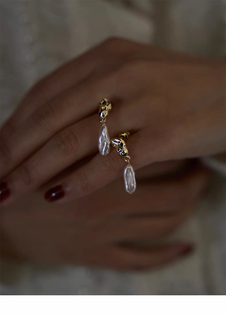 Gold and pearl earrings on a blurred hand background