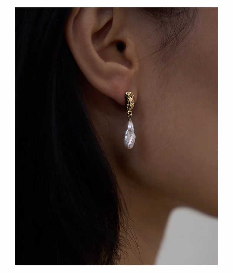 pearl earring with a gold setting worn by an ear against a neutral background