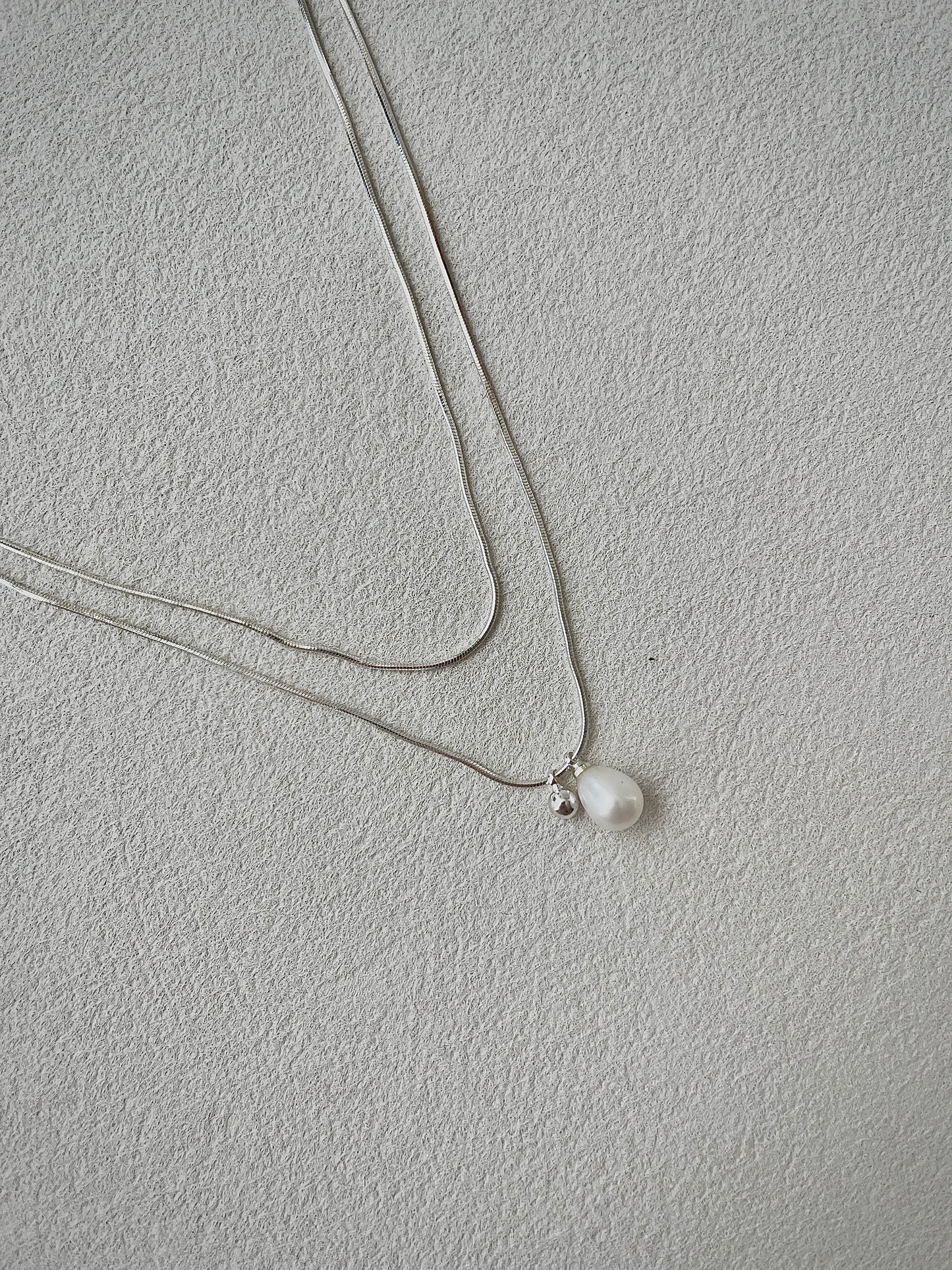 Necklace with a single pearl pendant on a light gray background