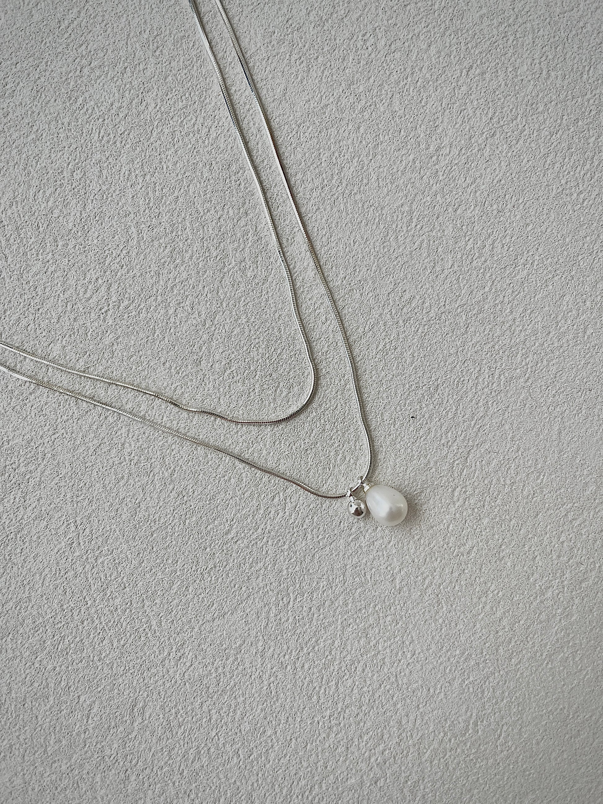 Necklace with a single pearl pendant on a light gray background