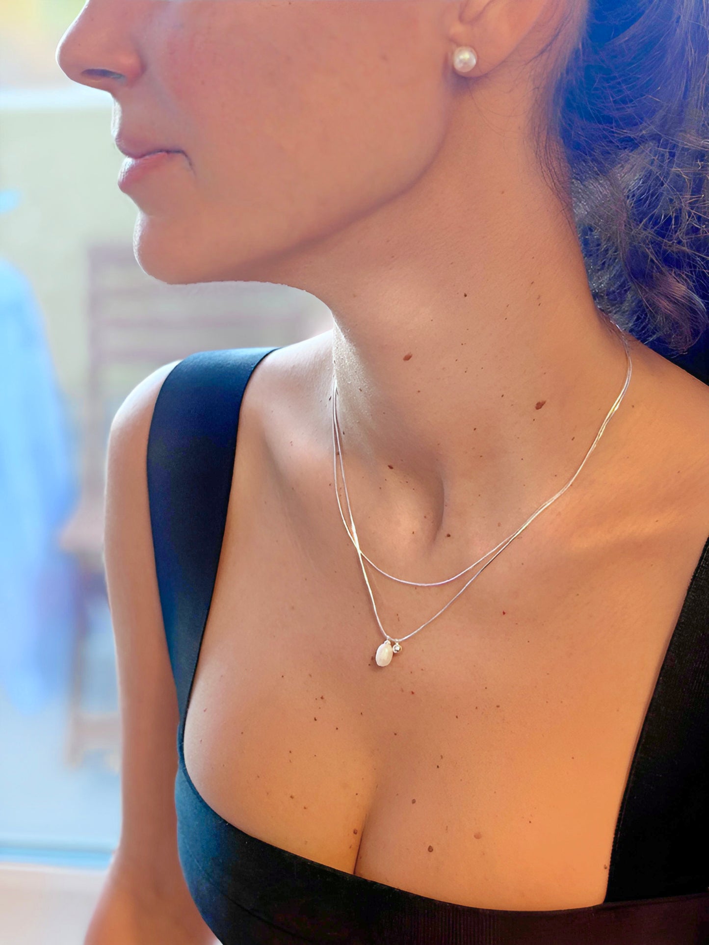 Close-up of a person wearing a silver necklace with a white pearl pendant.