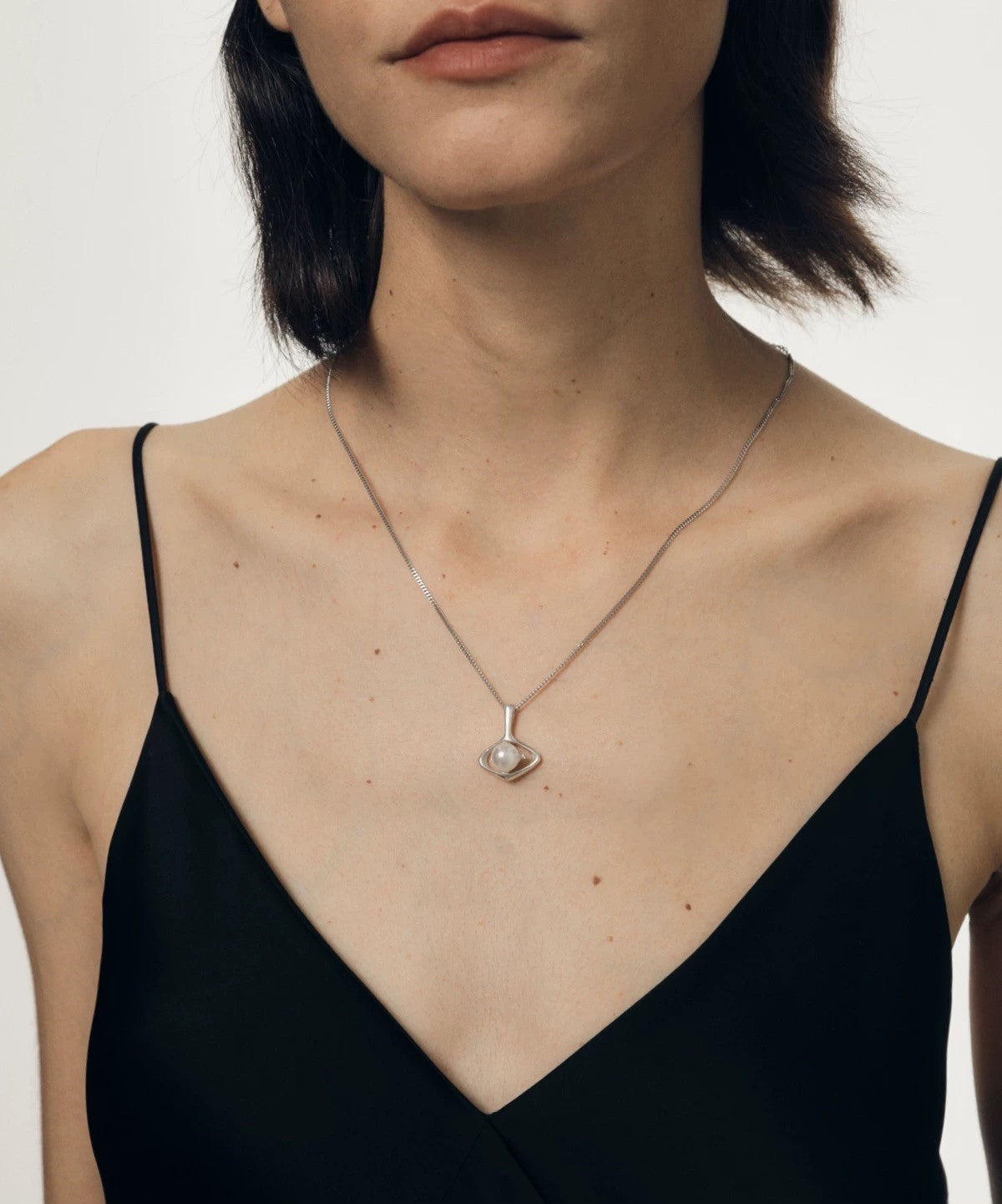 Woman wearing a black dress with a designer pearl pendant necklace against a neutral background