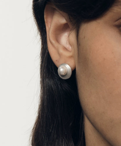 Close-up of an ear wearing a pearl earring with a plain background