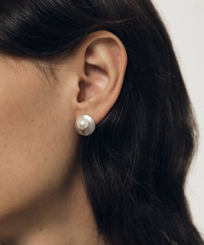 Close-up of an ear wearing a pearl earring with dark hair and neutral background