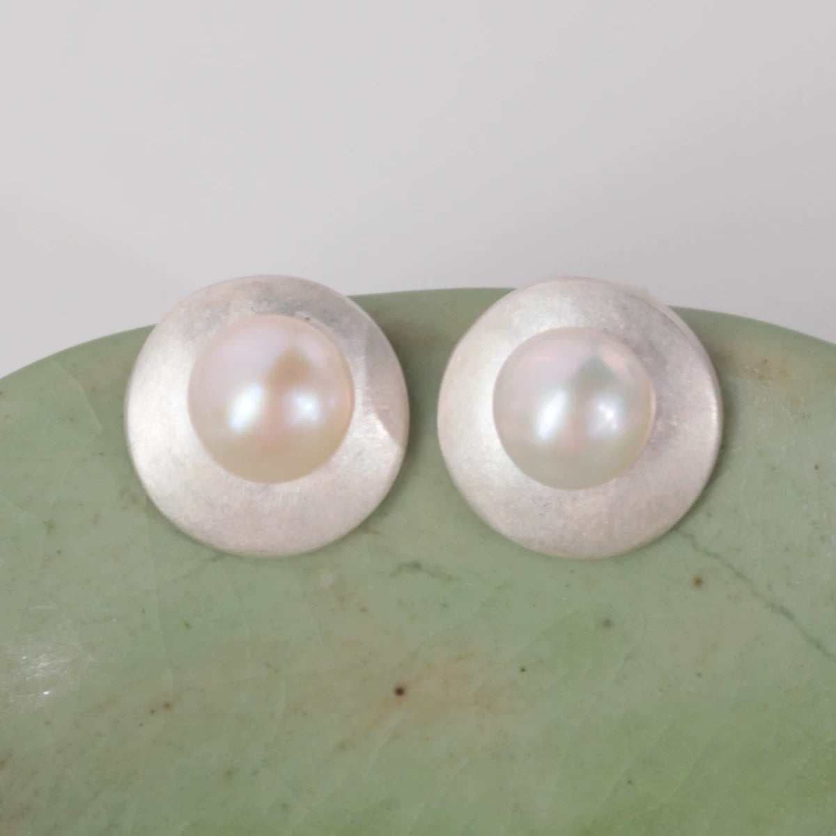 Pair of pearl earrings on a textured green surface