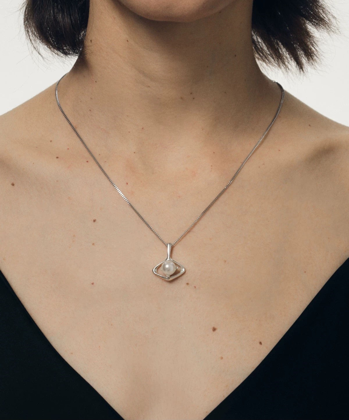 Silver necklace with a designer pearl pendant worn by a person against a neutral background