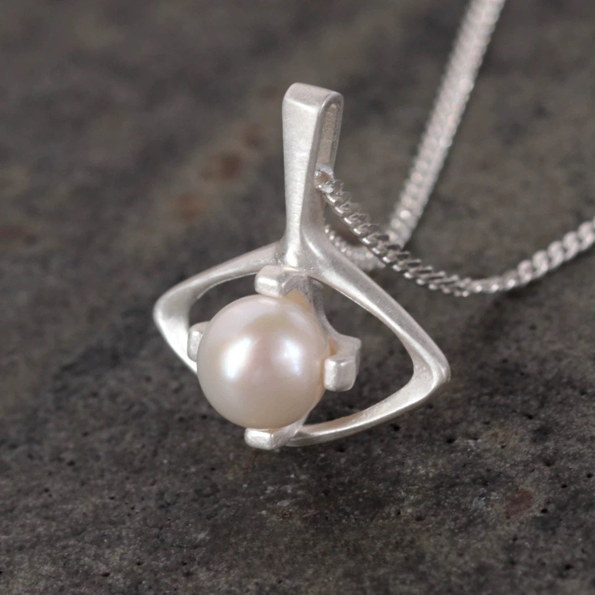 Silver pendant with a pearl on a dark textured surface