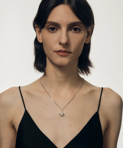 Woman wearing a black strappy top and a delicate necklace with a pearl pendant on a plain background