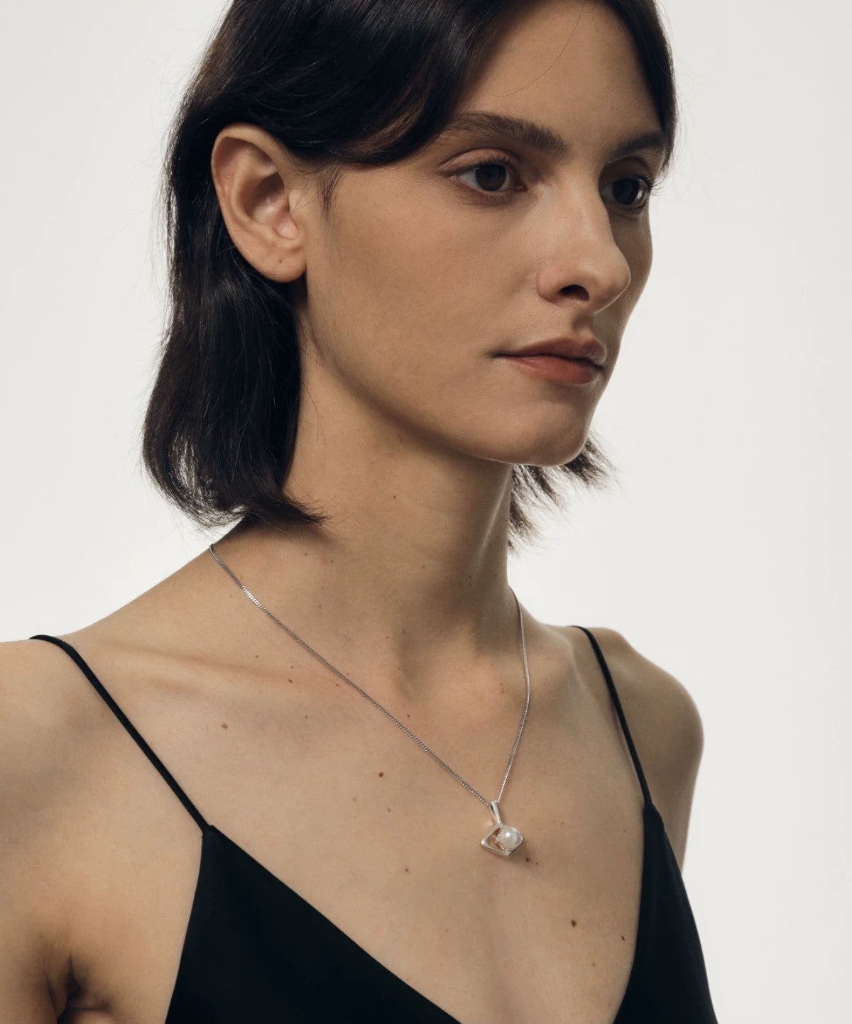 Woman wearing a black top and silver necklace with a designer pearl pendant on a white background