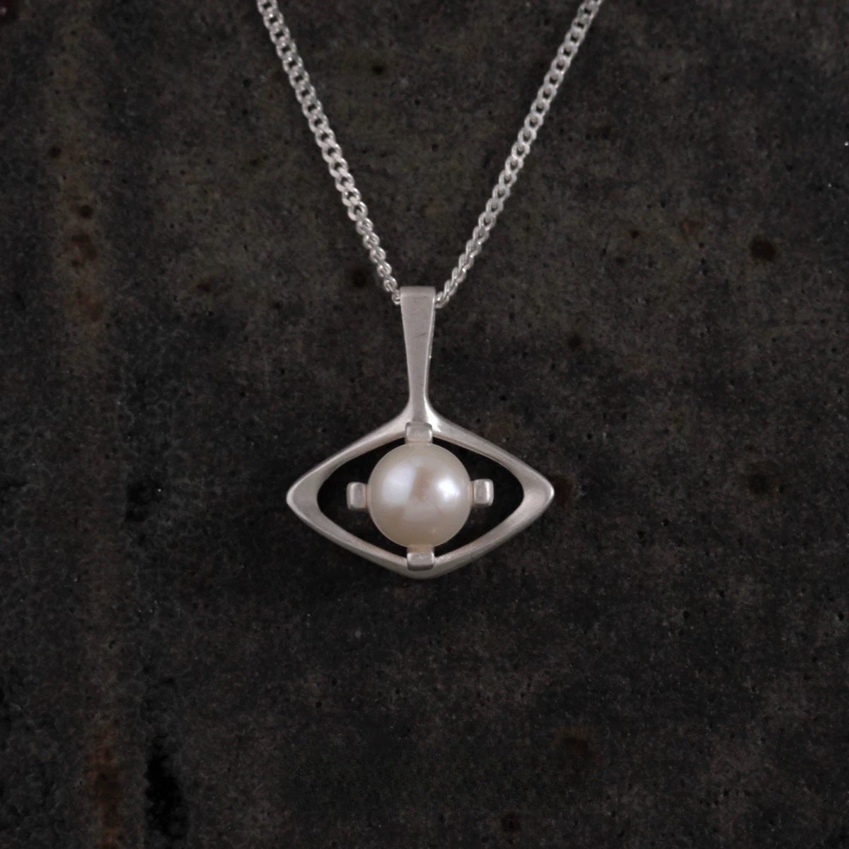 Silver necklace with a pendant featuring a pearl on a dark textured background