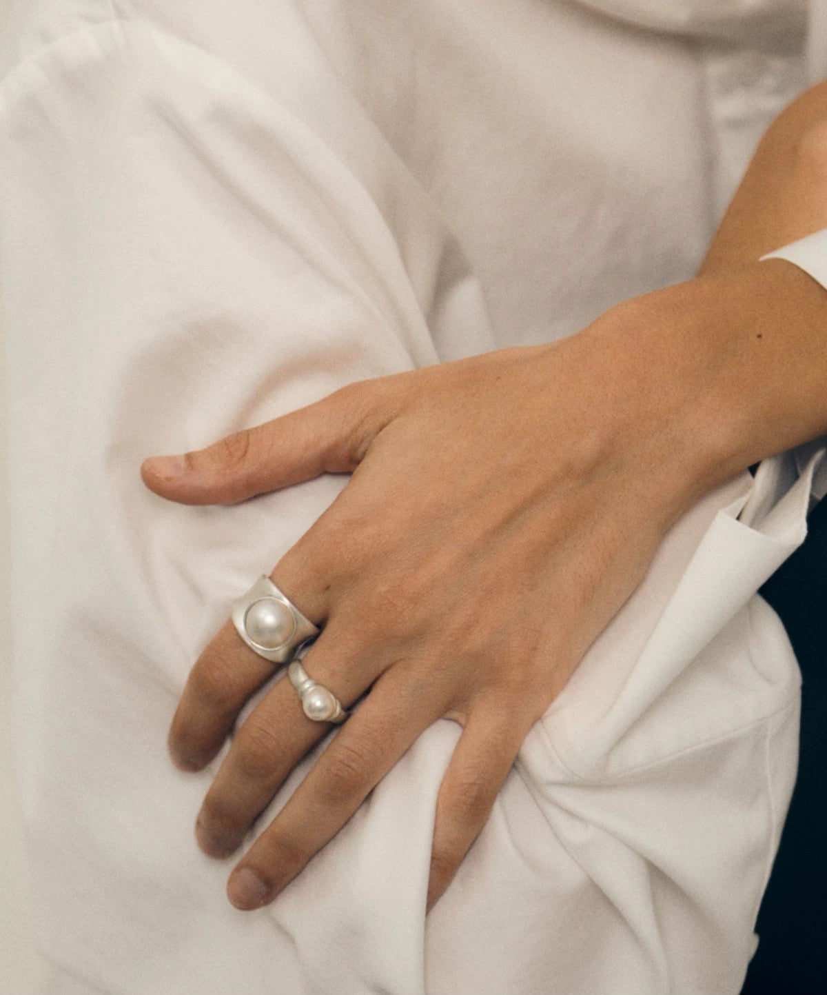 Hand wearing a silver ring with a pearl on a white fabric background