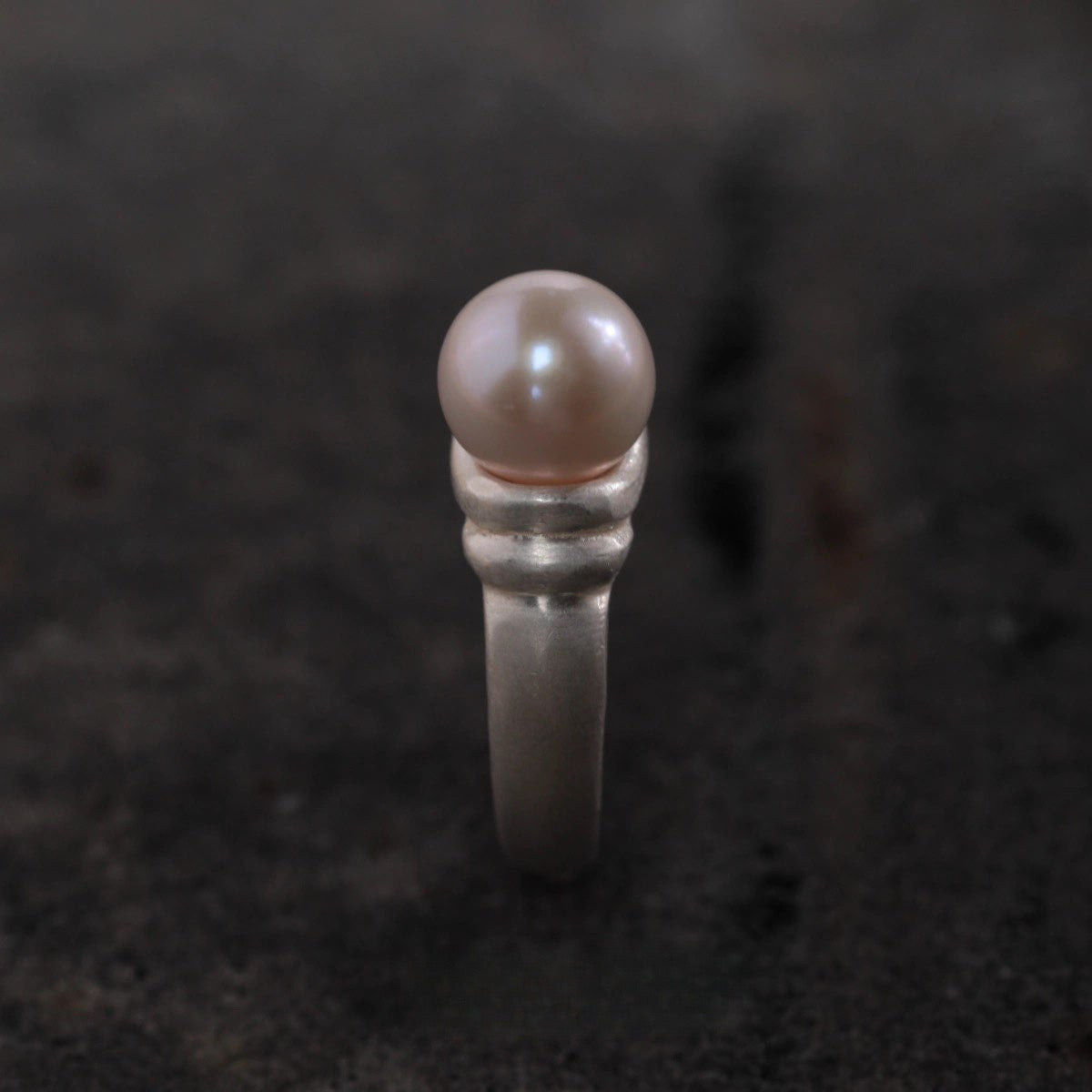 Silver ring with a pearl on a dark textured background