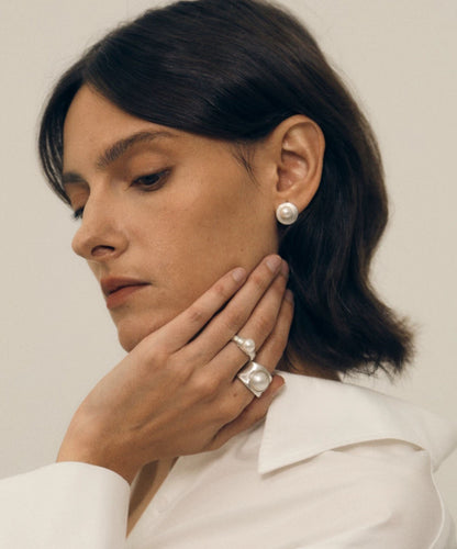Woman wearing pearl earrings and ring, looking down with a neutral expression.