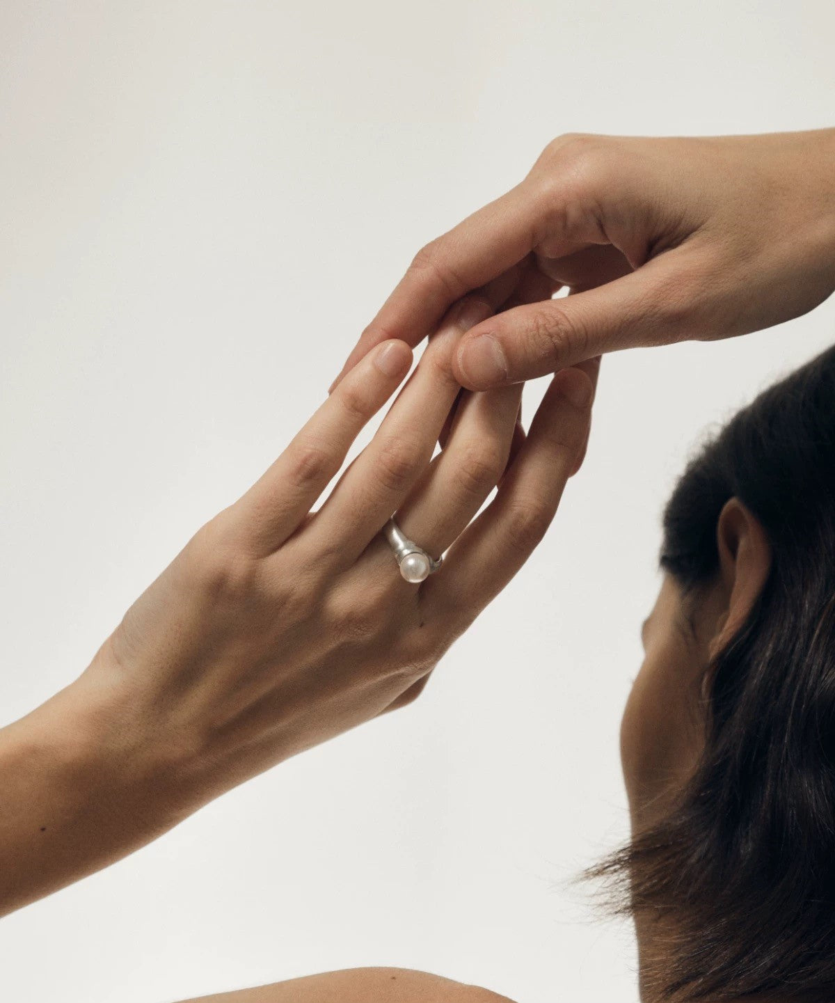 Close-up of a hand wearing a ring on a plain background