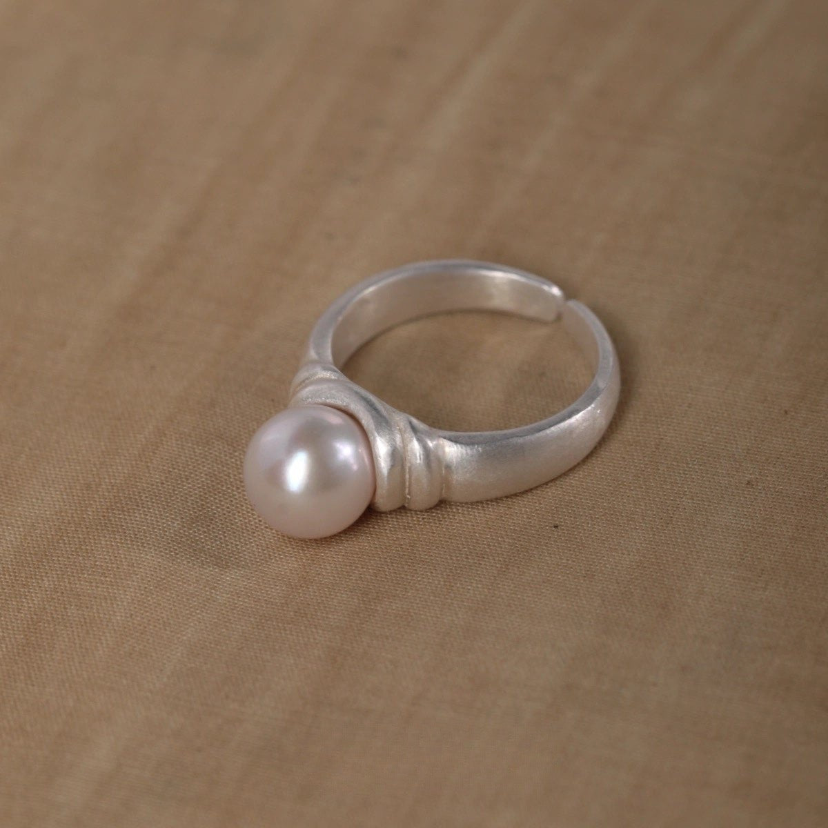 Silver ring with a pearl on a beige fabric background
