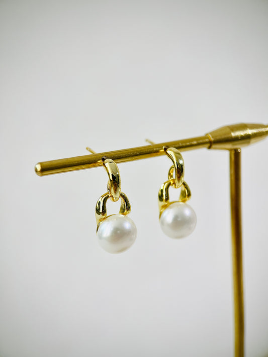 Gold earrings with pearl drops on a gold stand against a light gray background