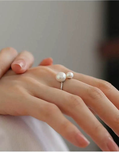 Hand wearing a ring with two pearls on a neutral background