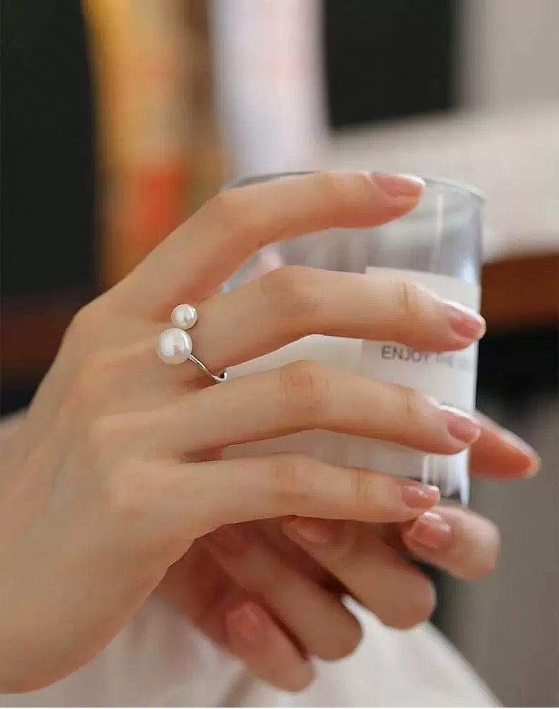 Hand holding a glass with a pearl ring on a blurred background