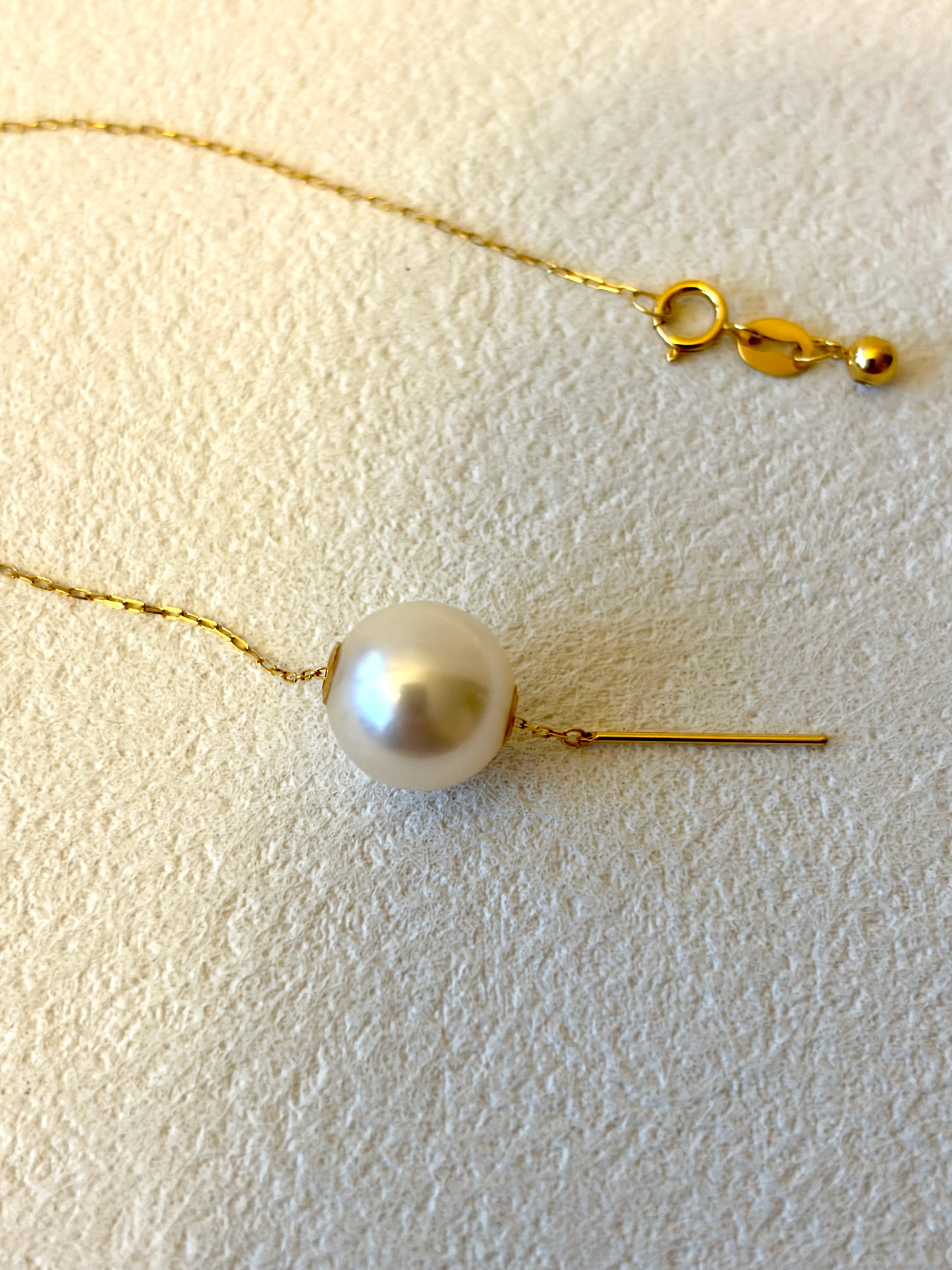Pearl necklace with gold chain on a textured white surface