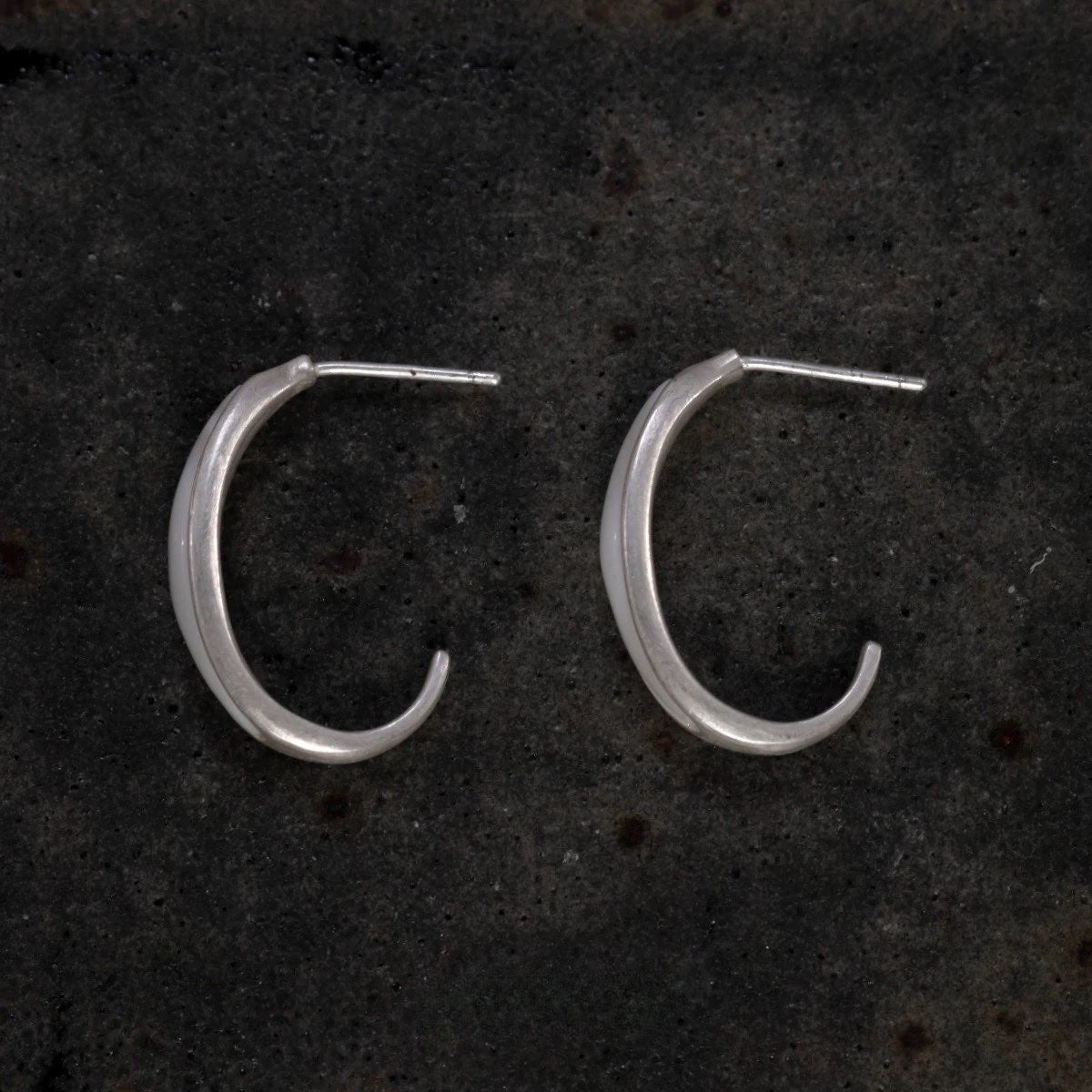 Silver hoop earrings on a dark textured surface