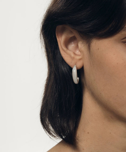 Close-up of a person wearing a silver hoop earring on a plain background