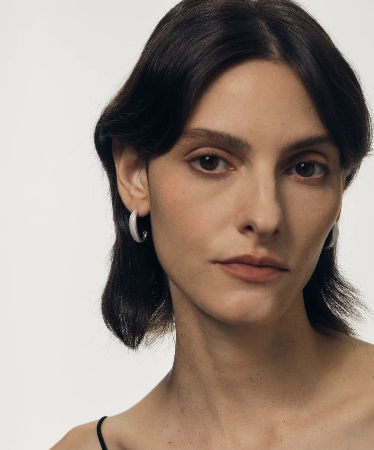 Woman with dark hair and hoop earrings against a plain background