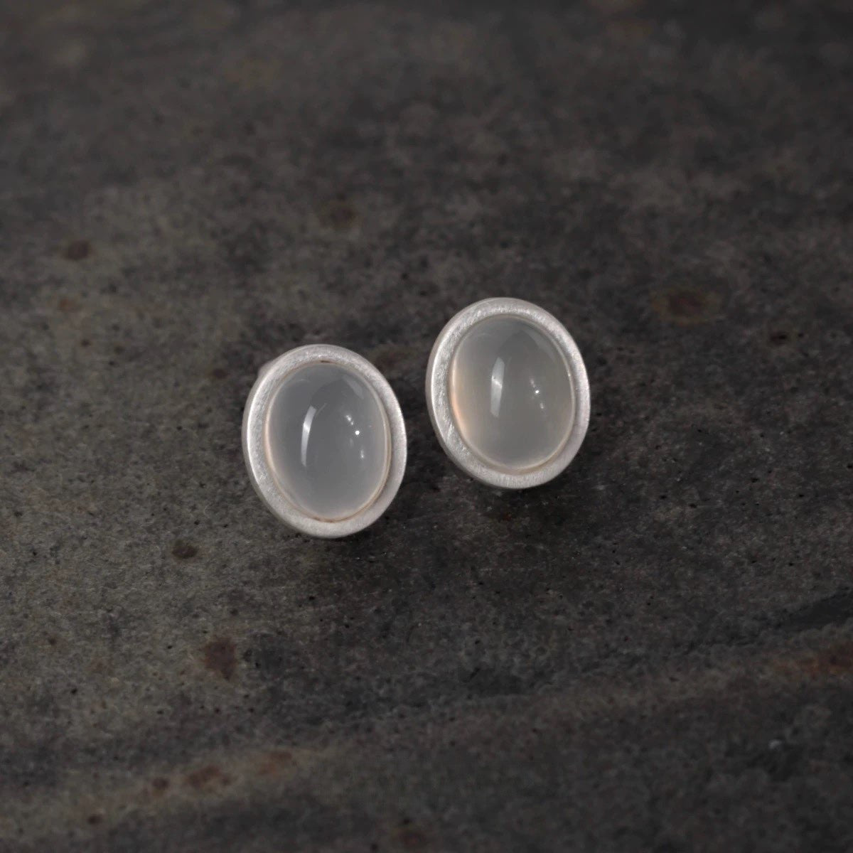 Pair of silver earrings with round stones on a dark textured surface