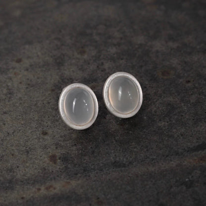 Pair of silver earrings with round stones on a dark textured surface