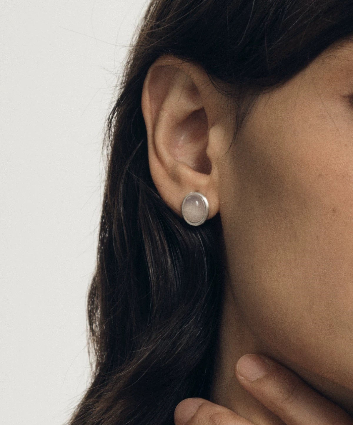 Close-up of an ear wearing a silver earring with a clear gemstone on a plain background