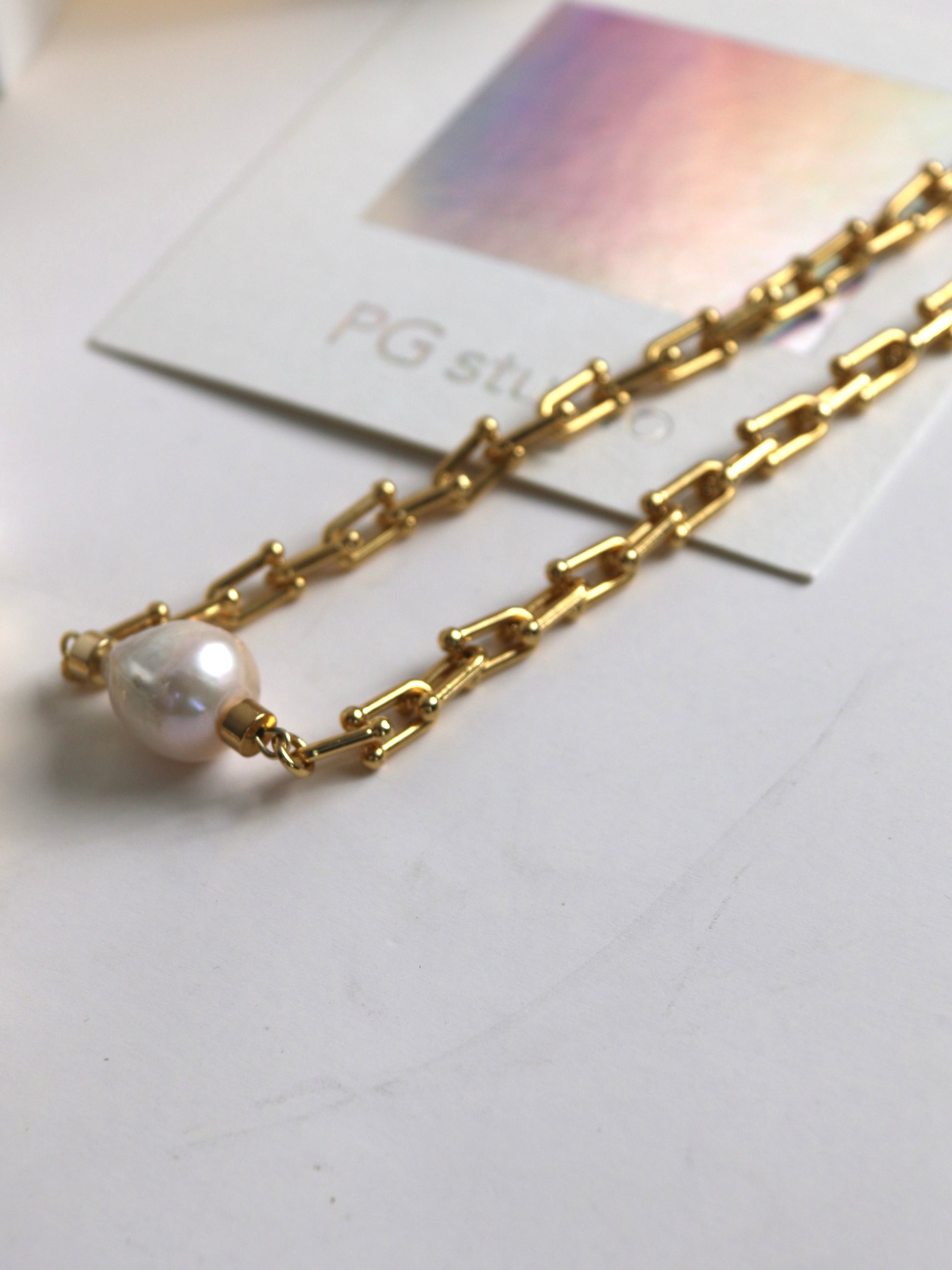 Gold chain necklace for men with a pearl on a white surface