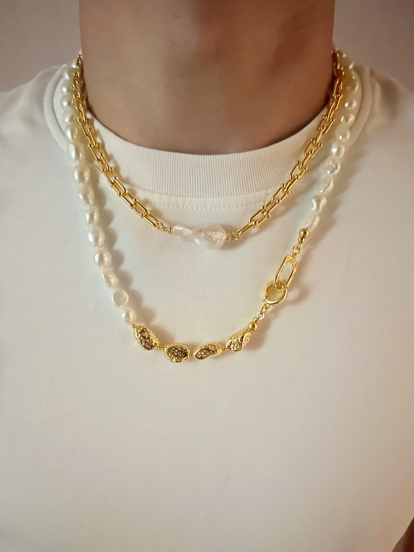 Gold chain necklace with baroque pearl pendant on a plain background