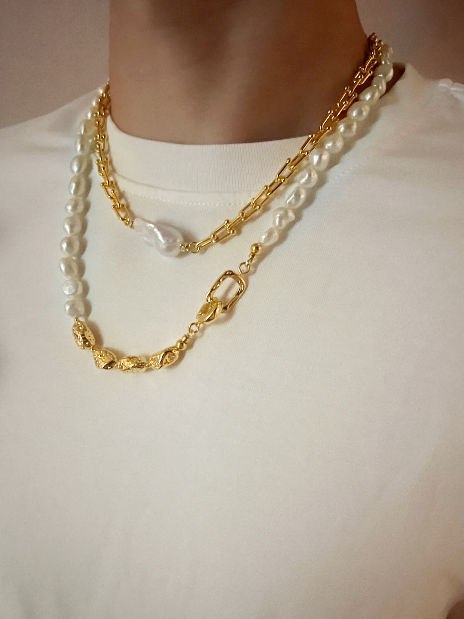Gold chain and pearl necklace on a plain background