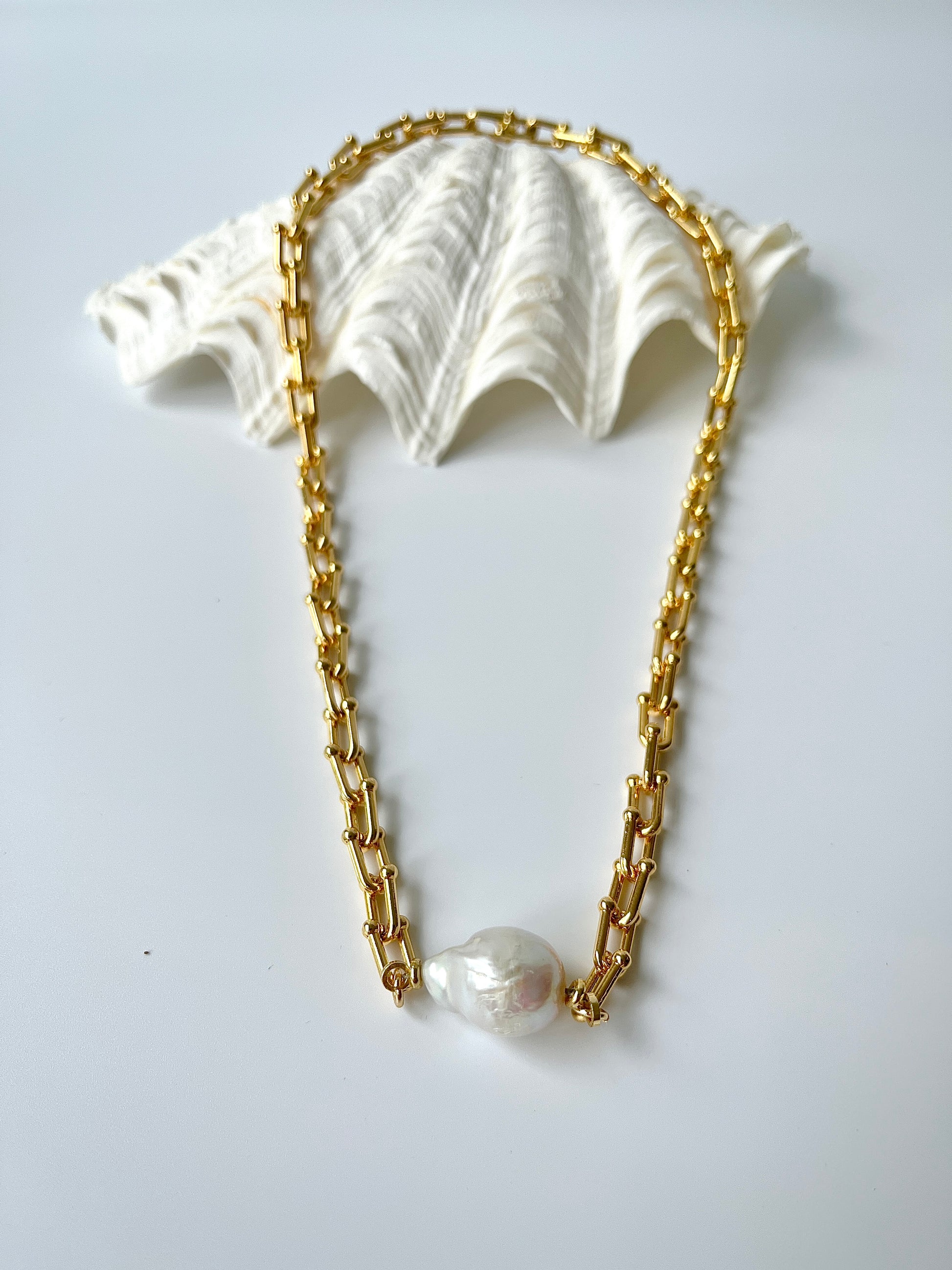 Gold chain necklace with white freshwater pearl pendants on a light gray background