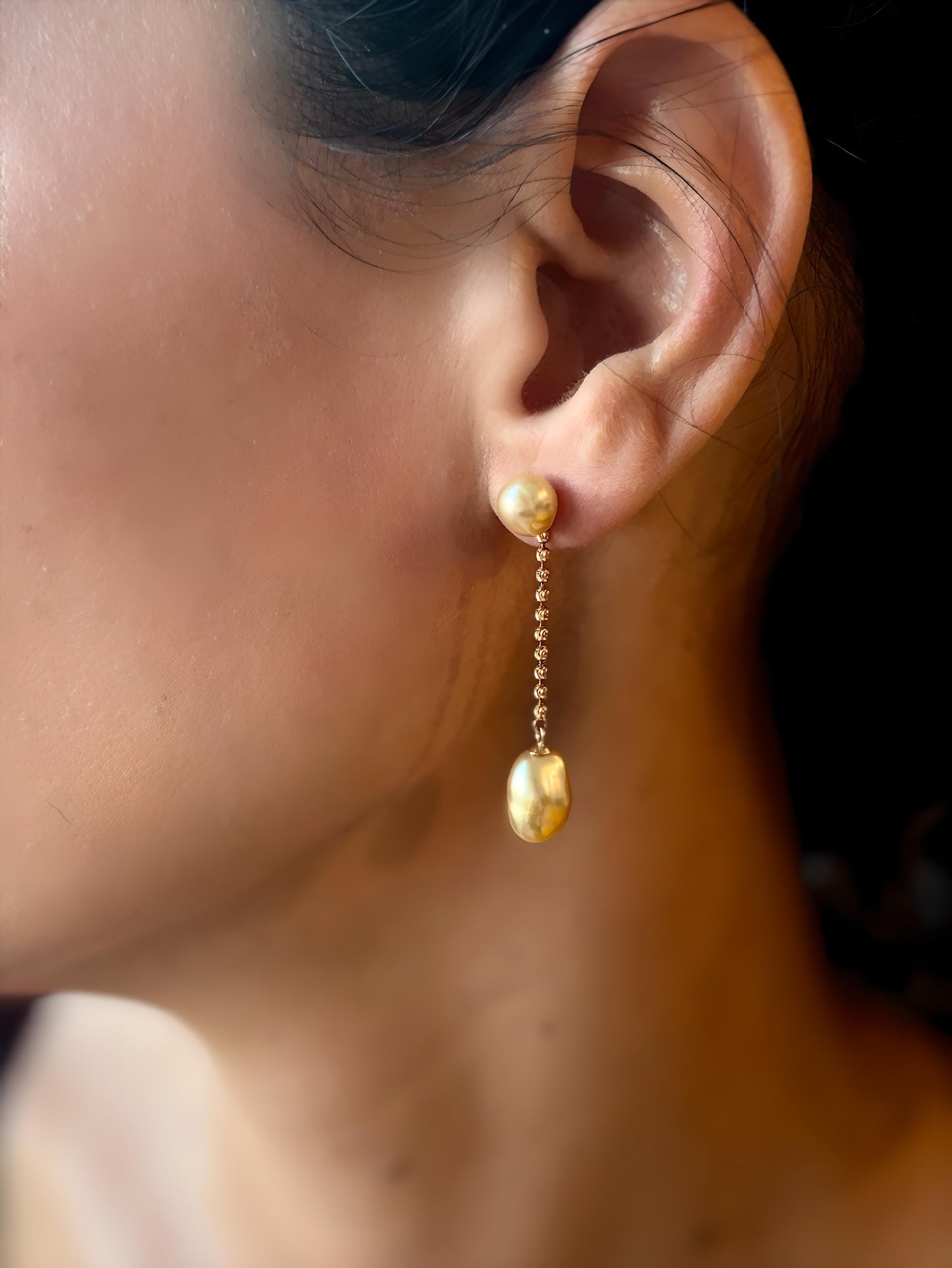 Woman with dark hair, wearing south sea golden pearl earrings, featuring Keshi pearls and 18K solid gold