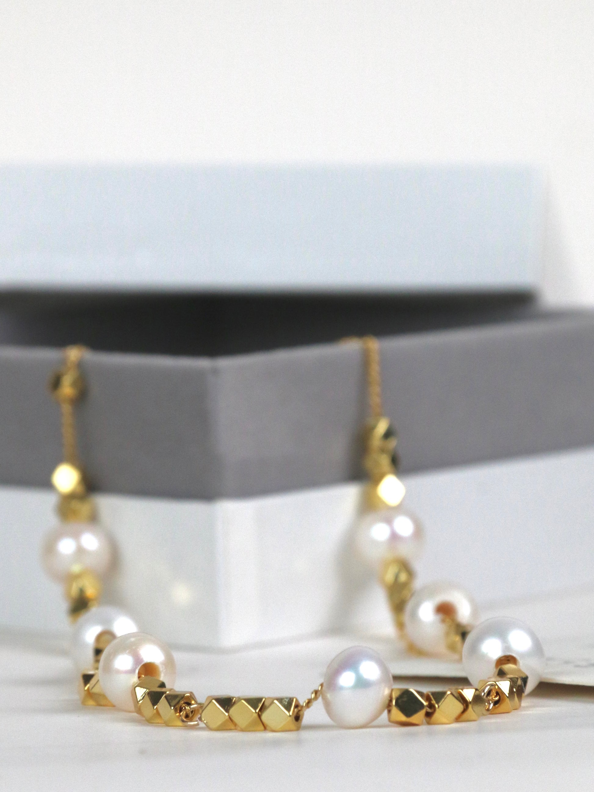 Gold and pearl necklace for men on a white surface with a gray stand in the background