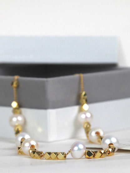 Gold and pearl necklace for men on a white surface with a gray stand in the background