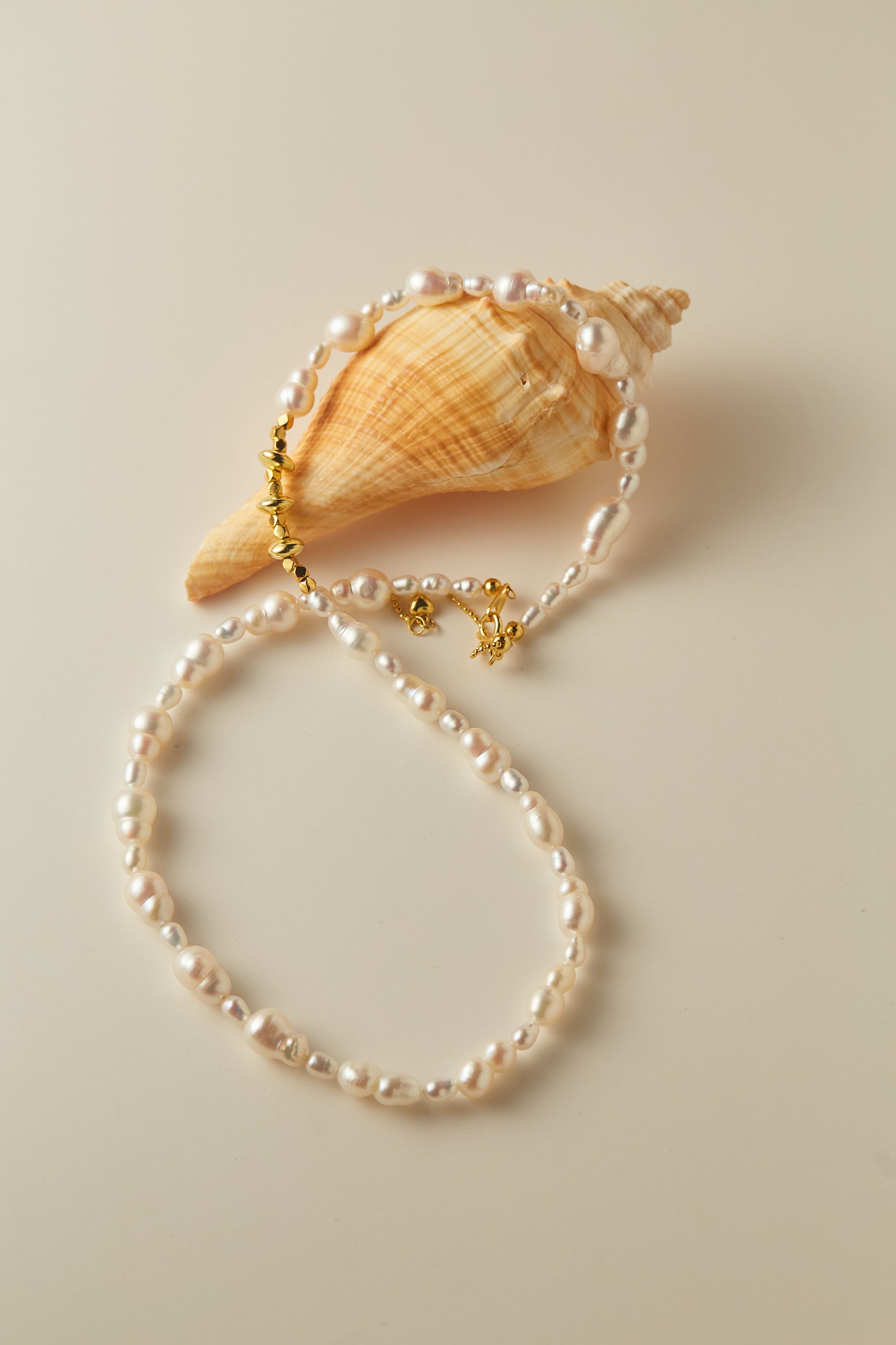 Pearl bracelet with gold clasp on a beige shell against a beige background