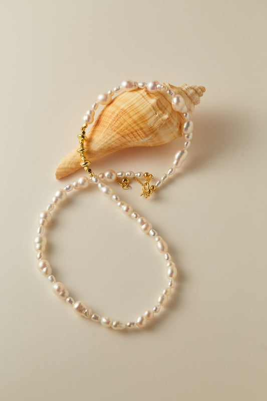 Pearl bracelet with gold clasp on a beige shell against a beige background