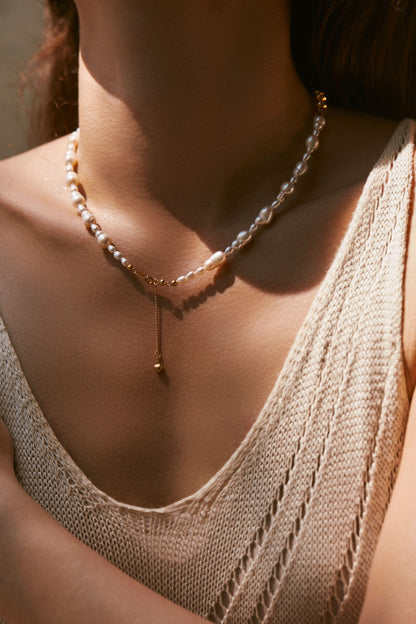 Close-up of a person wearing a delicate pearl necklace with a neutral background