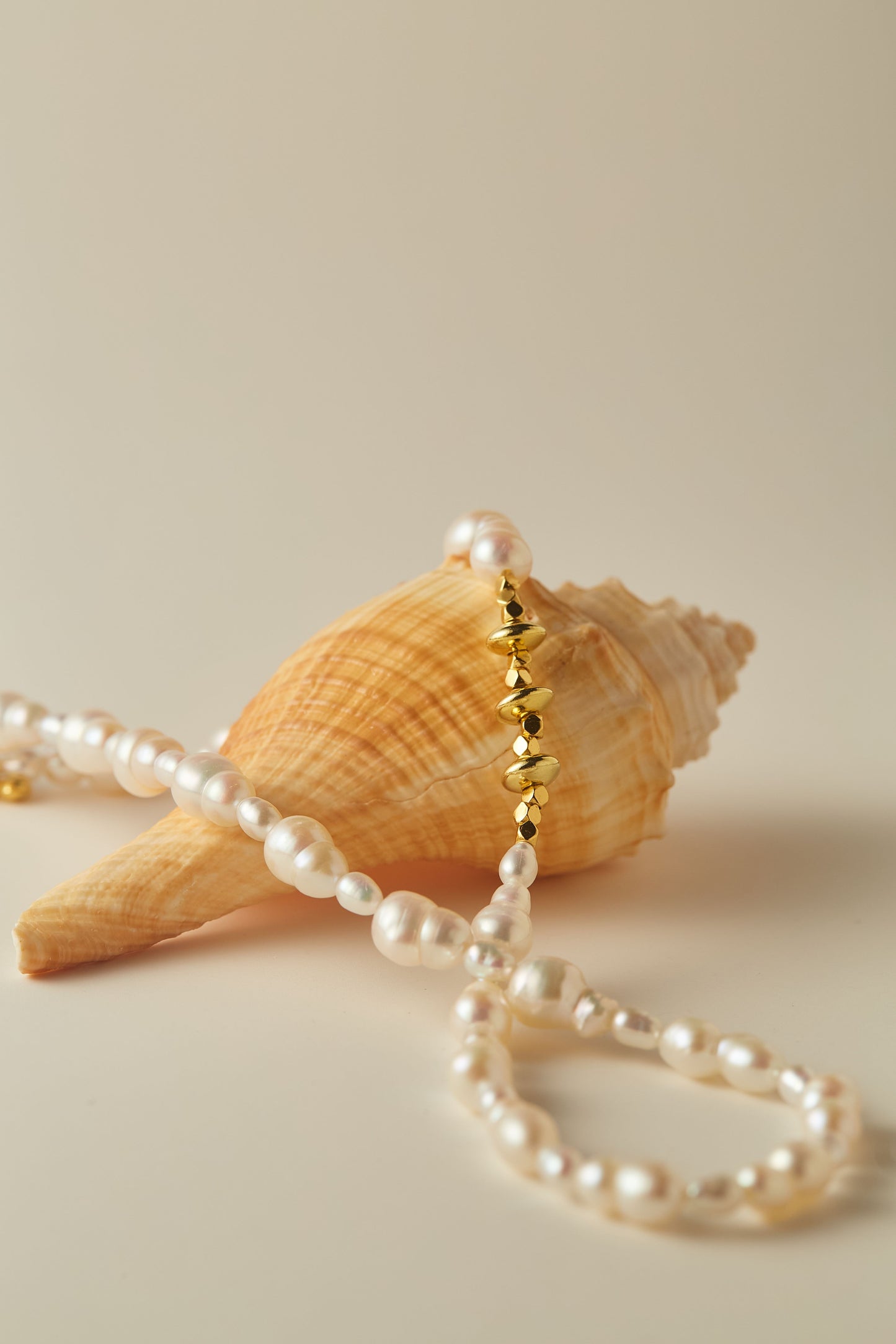 Pearl necklace with gold accents on a seashell against a beige background