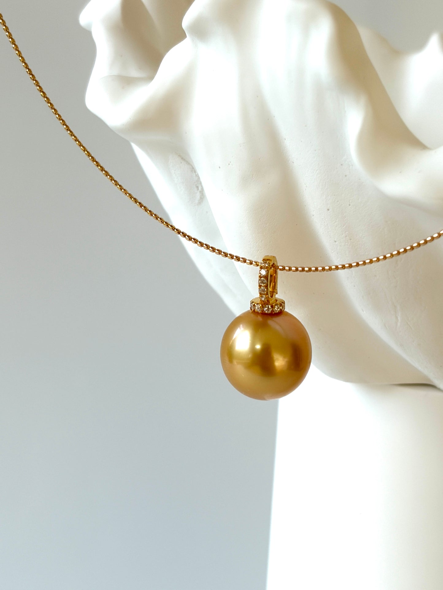 Gold choker with a large round golden  south sea pearl pendant on a white marble bust.