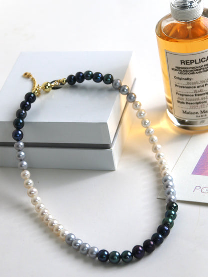 Necklace for men with black and white pearls next to a perfume bottle on a white surface