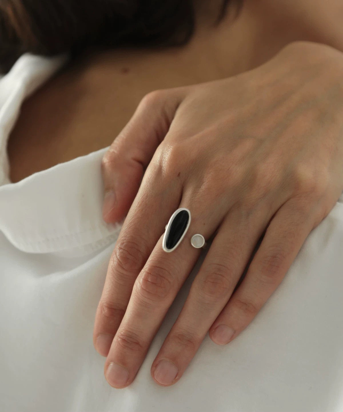 Hand wearing a black and silver ring on a white fabric background