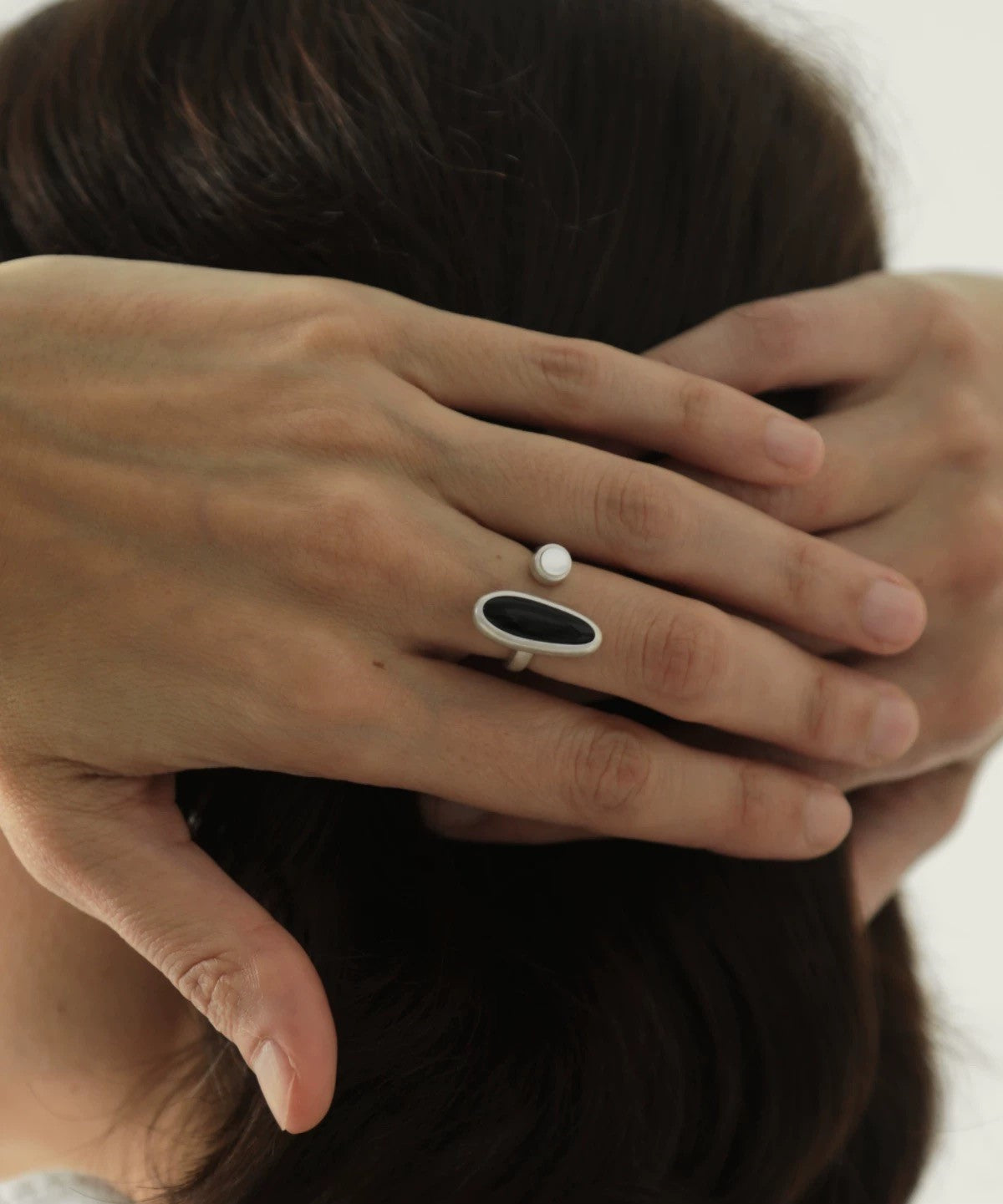 Close-up of a hand wearing a ring with a black and white design, holding hair.