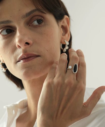 Woman wearing pearl earrings and a ring, with a plain background